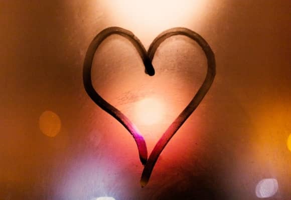 Heart drawn in window steam/fog. Warm yellow orange light coming from behind window