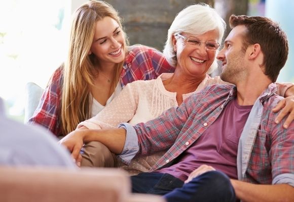 2 women one man. Family happy thinking bout memories. Young male and female with older grandmother in the middle. Young male and young femal wear plaid shirts of pink, purple and blue. older female wears white.