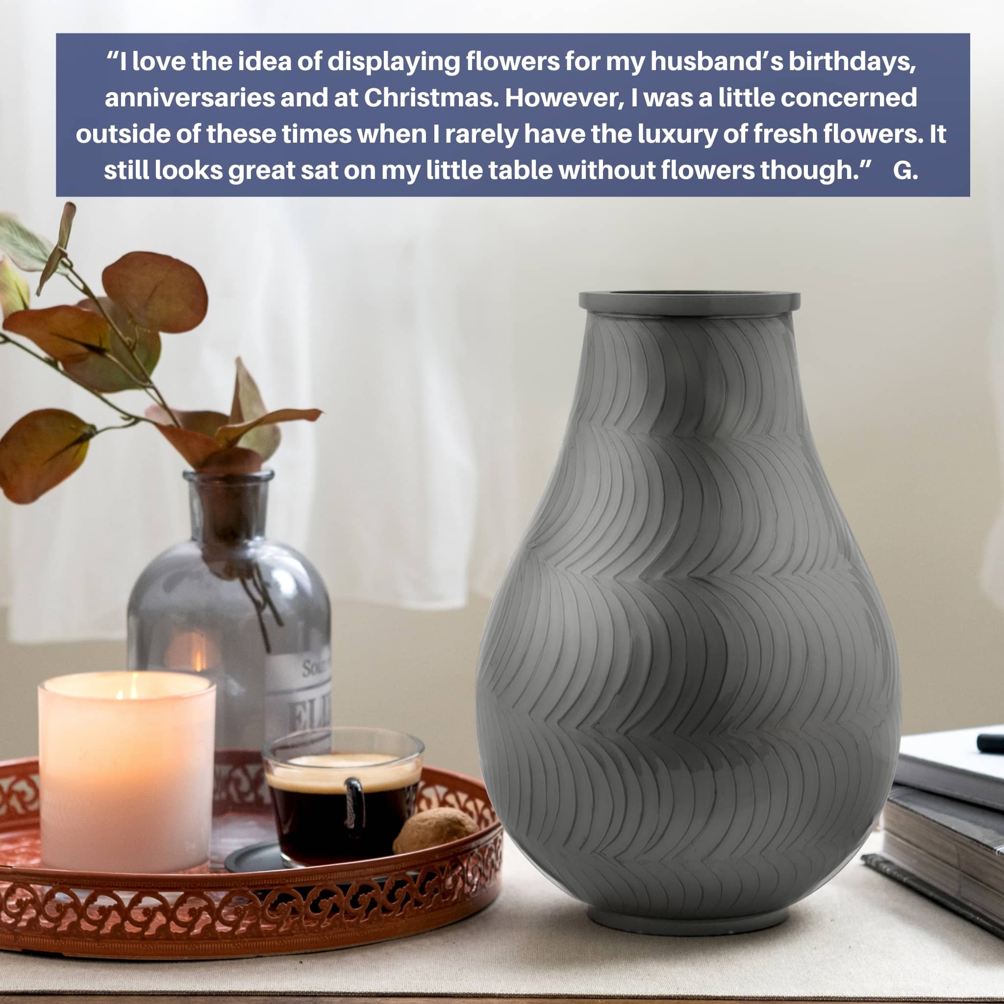 large ash urn for human ashes. silver gray cremation urn displayed on sideboard. candle, coffee and plant beside it.  books are plavced to right of the ashes urn