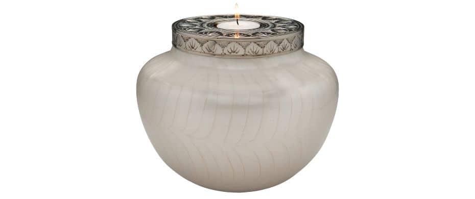 Large white candle cremation urn for human ashes with engraved silver lid.  Funeral urn is shownb on white background with a lit tea-light inside. The candle flame reflects of the silver lid with engraving. Main body of earn has pearlescent finish i