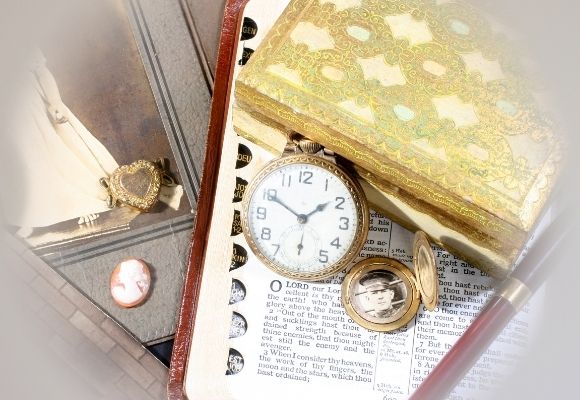 picture of some Momentos and keepsake of a loved one. Gold pocket watch, necklace,  gold jewelry photo necklace locket bible photograph gold notebook sits on top 