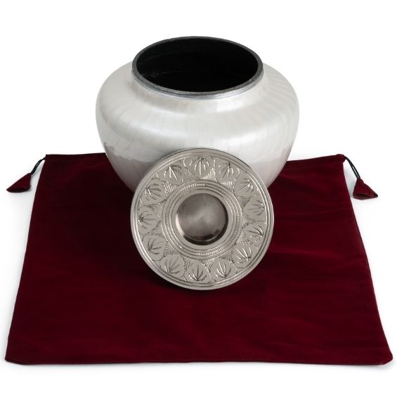 Large metal Cremation urn for ashes. Aluminum cremation Urn is displayed with lid removed sat on red velvet urn bag with drawstrings.  Funeral urn is white mother of pearl which looks ceramic and has a silver metal engraved lid with built in candle holder