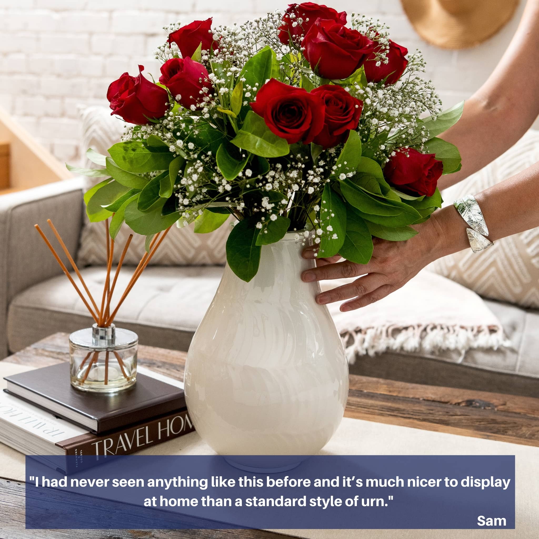 Large white cremation urn for human ashes displayed on wooden table. floral boquet, red roses inside,  womans hands placing down., white furnished home background